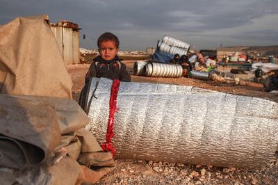 A child stands behind rolled-up thermal insulation foil out in the open at a camp for displaced Syrians east of Sarmada in the north of the northwestern Idlib province on February 16, 2020, as people prepare to flee the camp.
  / AFP / AAREF WATAD

