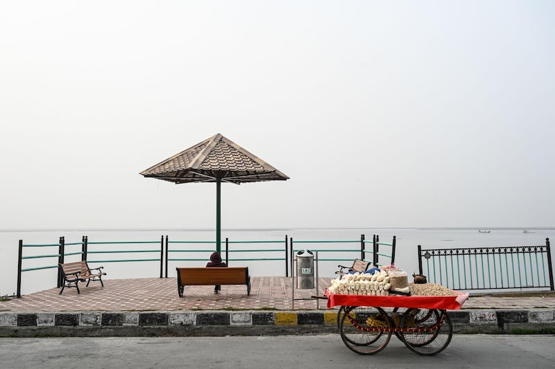 A roadside vendor sits on a bench on the banks of the Dal Lake amid dense fog  in Srinagar. AFP