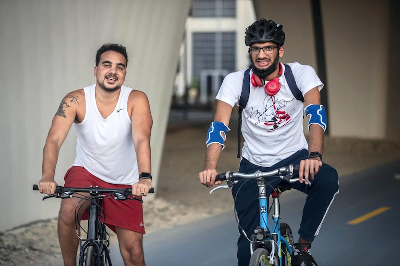 DUBAI, UNITED ARAB EMIRATES. 16 SEPTEMBER 2020. Shaddy Gaad (white vest) and his autistic buddy Omar Al Hashimi (Riding helmet) while cycling by the Creek in Business Bay. Since getting connected through the Rab3i platform which pairs people of determination with regular people who share their interested so they can have normal friends, they have been going out every 10 days to activities like cycling, swimming, playing video games and so on. (Photo: Antonie Robertson/The National) Journalist: Haneen Dajani. Section: National.