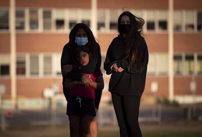Two women and a girl listen as a group of youths drum and sing outside the former Kamloops Indian Residential School, in honor of the 215 children whose remains have been discovered buried near the facility, in Kamloops, British Columbia, Friday, June 4, 2021. (Darryl Dyck/The Canadian Press via AP)