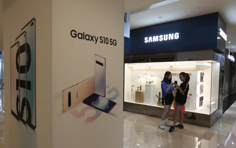 Middle school students watch their smartphones next to an advertisement of Samsung Electronics' Galaxy S10 5G smartphone at its shop in Seoul, South Korea, Tuesday, April 30, 2019. Samsung Electronics Co. says its operating profit for the last quarter declined more than 60% from a year earlier because of falling chip prices and sluggish demands for its display panels. (AP Photo/Ahn Young-joon)