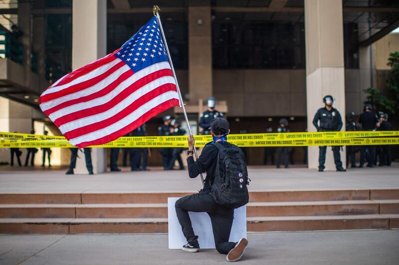 A demonstrator holding a US flag kneels in front of the police at the Anaheim City Hall in Anaheim, California, during a peaceful protest over the death of George Floyd.   AFP