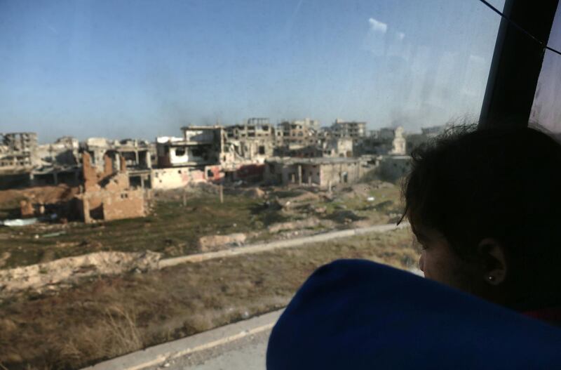 A convoy transporting Syrian civilians and rebel fighters drives past destroyed buildings in Arbin in Eastern Ghouta as they are evacuated from the opposition enclave to the village of Qalaat al-Madiq, some 45 kilometres northwest of the central city of Hama, on March 25, 2018. Abdulmonam Eassa / AFP