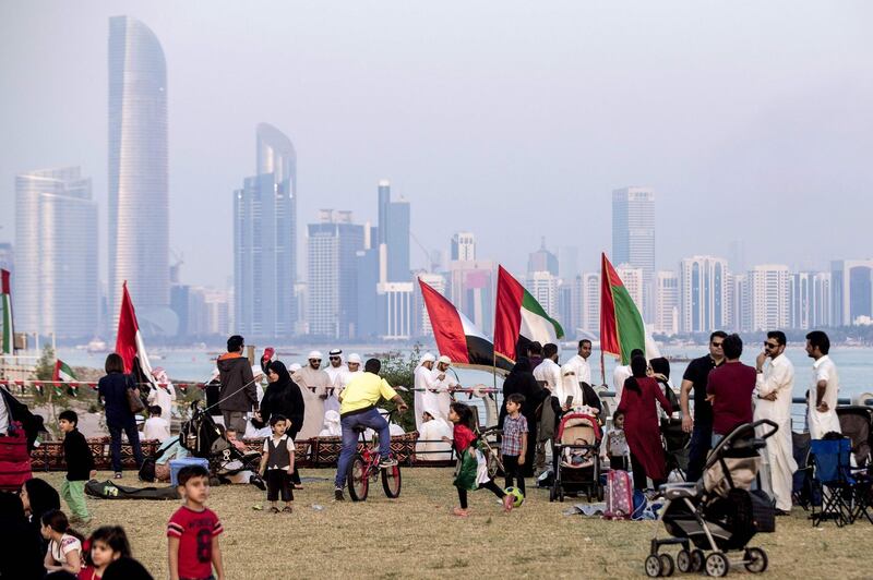 Children play along the corniche as spectators gather to watch UAE's Al-Fursan (The Knights) National Aerobatic Team performing in the capital Abu Dhabi on December 1, 2017, during celebrations ahead of the 46th Emirati National Day, celebrated on December 2. / AFP PHOTO / NEZAR BALOUT