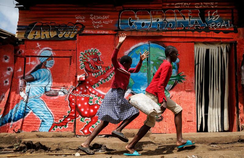 Children run down a street past an informational mural warning people about the dangers of coronavirus in the Kibera slum of Nairobi, Kenya on Wednesday, June 3, 2020. AP Photo