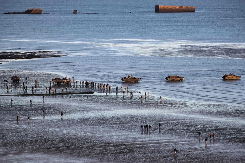 WWII enthusiasts walk near DUKW (colloquially known as Duck), a six-wheel-drive amphibious modification of the 2 1/2-ton CCKW trucks used by the US military, on the beach of Asnelles, in Normandy. APF