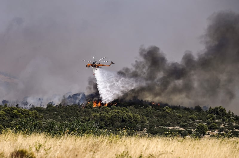 A helicopter sprays water to douse a fire in Dervenochoria, Greece. AFP