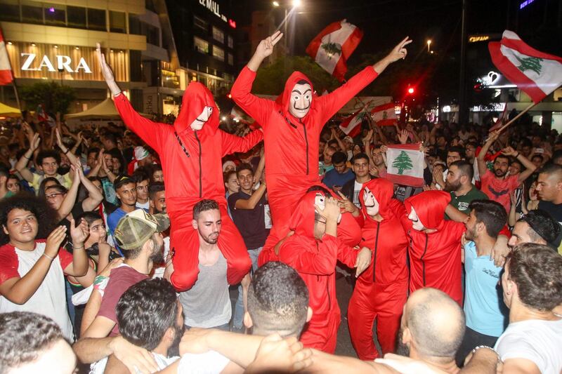 Lebanese protesters, wearing the masks of the Spanish TV show "La Casa de Papel", dance during a protest against dire economic conditions in the Lebanese southern port city of Sidon (Saida), on October 19, 2019. Tens of thousands of Lebanese people took to the streets today for a third day of protests against tax increases and alleged official corruption despite several arrests by security forces. / AFP / Mahmoud ZAYYAT
