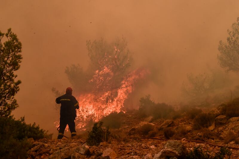 Locals help a firefighter as they try to extinguish a wildfire burning near the village of Vlyhada near Athens. Getty Images