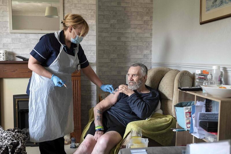 Team leader for housebound vaccinations, Julie Fletcher administers a dose of AstraZeneca/Oxford Covid-19 vaccine to housebound patient Graham Mullins at his home in Hasland, near Chesterfield, central England on April 14, 2021.  Prime Minister Boris Johnson has said that the UK had passed "another hugely significant milestone" after confirming a jab had been offered to all over-50s, the clinically vulnerable and health and social care workers, ahead of a self-imposed April 15 deadline.  / AFP / OLI SCARFF
