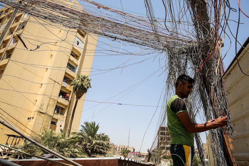 A man checks the wiring on electric cables reaching out to homes in Saadoun Street in the Iraqi capital Baghdad on July 29, 2018, as chronic power shortages have forced residents to buy electricity from private entrepreneurs who run generators on street corners across the country. - Iraqi Prime Minister Haider al-Abadi sacked his minister of electricity on July 29 after three weeks of protests against corruption and chronic power cuts in the energy-rich country where successive conflicts have devastated infrastructure. (Photo by SABAH ARAR / AFP)