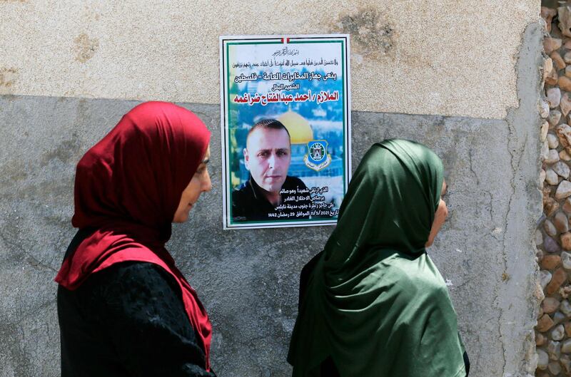 Relatives of Ahmed Daraghmeh, a member of Palestinian intelligence services who was killed by Israeli forces the previous day at the Zaatara (Tapuach) junction south of Nablus in the occupied West Bank, stand by a poster depicting him displayed on a wall as they mourn during his funeral in the town of al-Lubban al-Sharqiya near Nablus on May 12, 2021. Daraghmeh, 30, was killed and another Palestinian wounded by Israeli army gunfire in the north of the occupied West Bank as violence soared between Israel and the Palestinian territories. Both were shot at an Israeli army checkpoint near Nablus. The Israeli army earlier reported an "attempted drive-by shooting at Tapuah Junction" near Nablus. / AFP / ABBAS MOMANI
