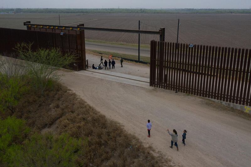 Migrants await transport as Sonia, an asylum seeker from Honduras, arrives at the border wall with her three children Jefferson, 9, Scarlet, 7, and David, 6, after they crossed the Rio Grande river into the United States from Mexico on a raft in Penitas, Texas, U.S., March 16, 2021. Picture taken with a drone. REUTERS/Adrees Latif