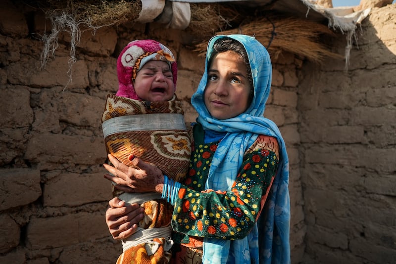 Qandi Gul holds her brother outside their home in a camp for those displaced by war and drought near Herat.  Qandi's father sold her into marriage without telling his wife, taking a down payment so he could feed his family of five children.  AP Photo