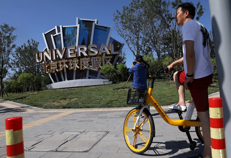 A man uses a bike-sharing service near a giant sign for Universal Beijing Resort, ahead of its opening. Reuters