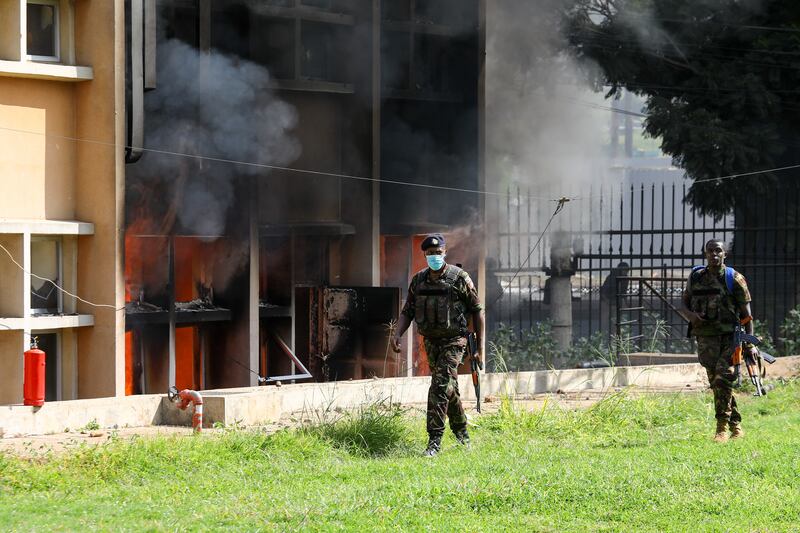 Armed Kenyan officers walk past flames and smoke coming out of a burning building, part of the Parliament building. EPA