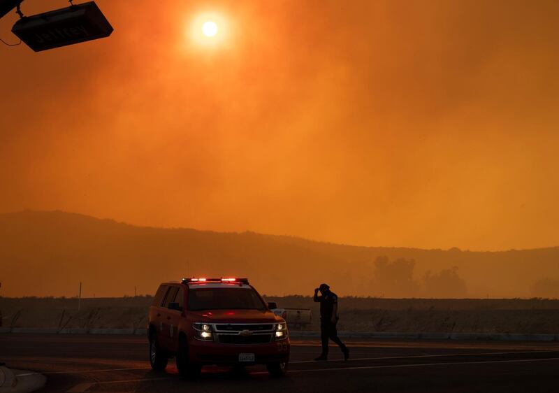Police and firefighters are out in full force on Jeffrey and Portola in Irvine, Calif., where smoke fills the sky from the wind-driven Silverado wildfire. The Orange County Register via AP