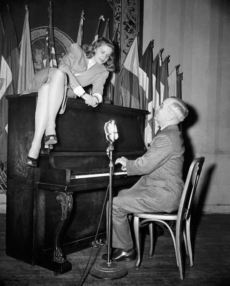 In this 1945 file photo, Vice President Harry S. Truman plays the piano as actress Lauren Bacall lies on top of it during her appearance at the National Press Club canteen in Washington. AP