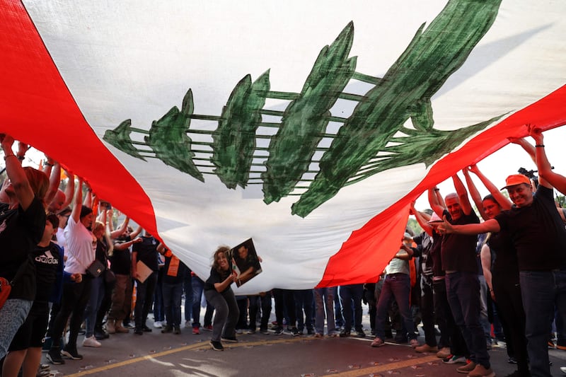 Supporters of Lebanon's President Michel Aoun cheer under a large national flag, as he prepares to leave the presidential palace in Babbda at the end of his mandate. AFP