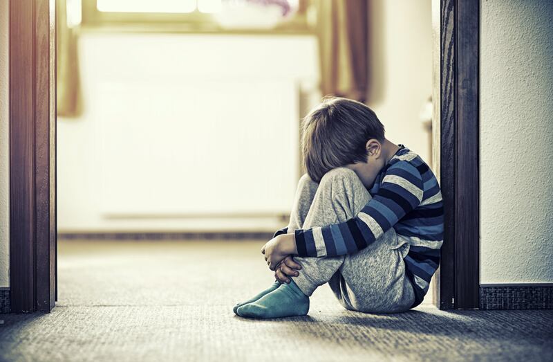 Depressed sad child sitting on the floor, in the door. The little boy is hiding his head between legs.