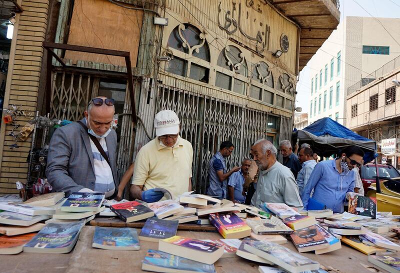 Iraqis check out books sold by a street vendor after measures of social distancing were eased by the authorities, ahead of the fasting month of Ramadan, in central Baghdad on April 22, 2020, during the novel coronavirus pandemic crisis.  / AFP / SABAH ARAR
