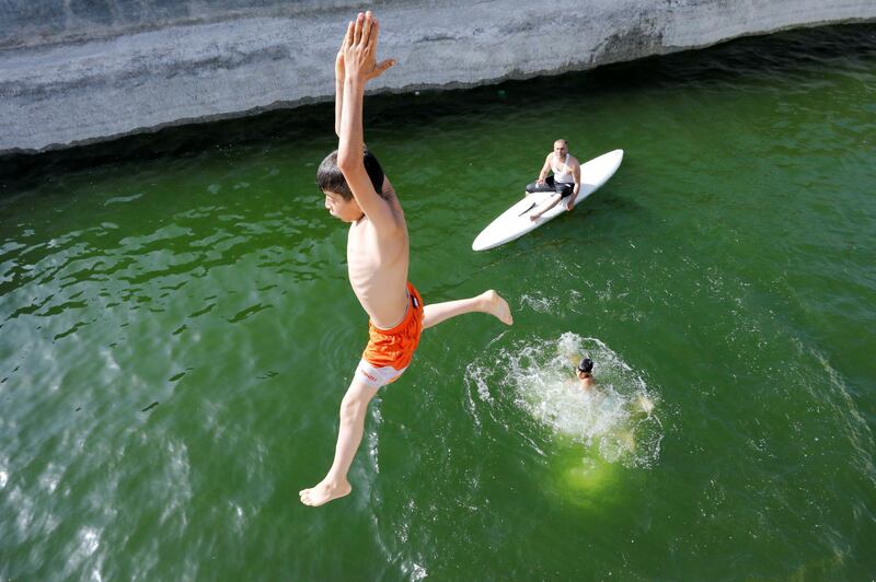 A boy jumps as Palestinian farmer Murad Abu Aram rides on a surfboard at his fish farm in a man-made pond in Hebron, in the Israeli-occupied West Bank. Reuters