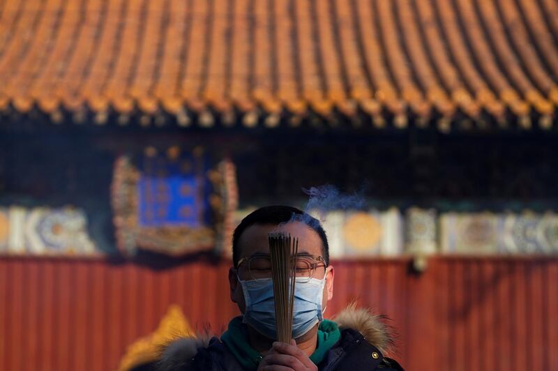 A man wearing a face mask to help curb the spread of the coronavirus holds incense offers prayers on the first day of the New Year at Yonghegong Lama Temple in Beijing. AP Photo