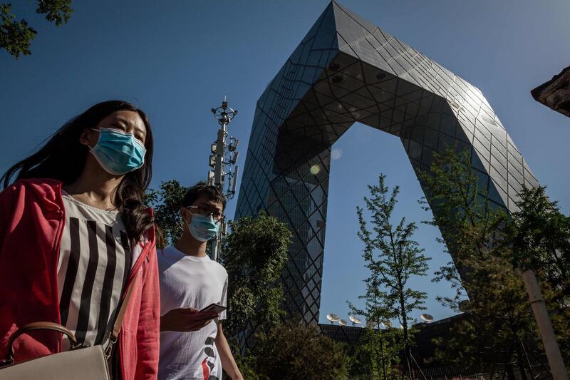 People wearing face masks walk past the CCTV building in Beijing on May 19, 2020. AFP