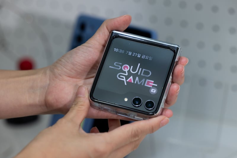 The Squid Game logo is displayed on a Galaxy Z Flip 5 smartphone
