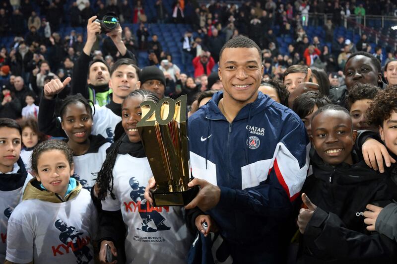 Kylian Mbappe poses with a trophy and children at the end of a ceremony after he became Paris Saint-Germain's all-time top scorer. AFP