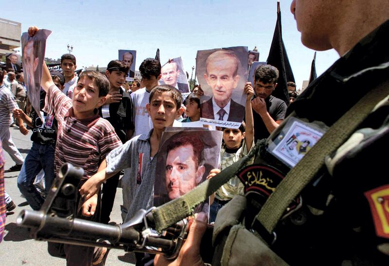 (FILES) In this file photo taken on June 12, 2000, a presidential guard watches Syrian youths as they march through the streets of the capital Damascus with portraits of late president Hafez al-Assad and his son Bashar. - President Bashar al-Assad, whose family has ruled Syria for over half a century, faces an election this week meant to cement his image as the only hope for recovery in the war-battered country, analysts say. (Photo by Patrick BAZ / AFP)