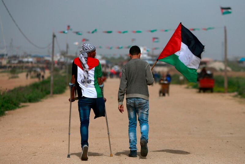 An amputee wearing a t-shirt depicting the colours of the Palestinian flag walks on crutches with another holding a Palestinian flag as they head towards a demonstration. AFP