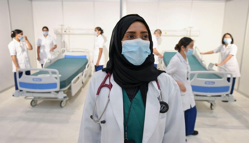 An Emirati doctor looks on as a nursing staff prepares beds in a huge field hospital being built by the government of Dubai in the United Arab Emirates, on April 14, 2020, with a capacity of more than 3000 patients at the Dubai international Convention and Exhibition Center amid the COVID-19 pandemic. / AFP / KARIM SAHIB
