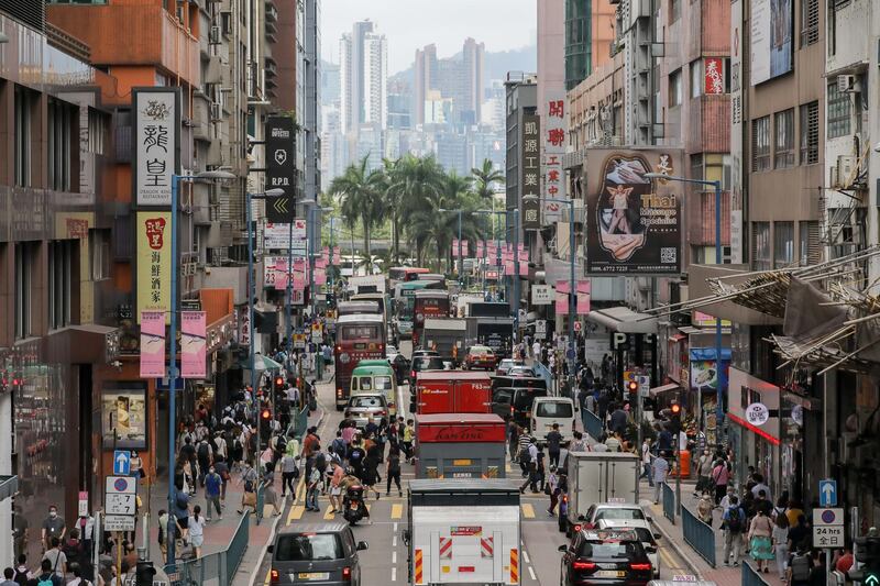 Pedestrians walk past vehicles in a street during the morning rush hour in the Kwun Tong district of Hong Kong, China, on Wednesday, May 6, 2020. Hong Kong leader Carrie Lam moved to loosen curbs on social gatherings and reopen shuttered schools, as a lull in coronavirus infections set the stage for fresh political battles over the future of the Asian financial hub. Photographer: Paul Yeung/Bloomberg