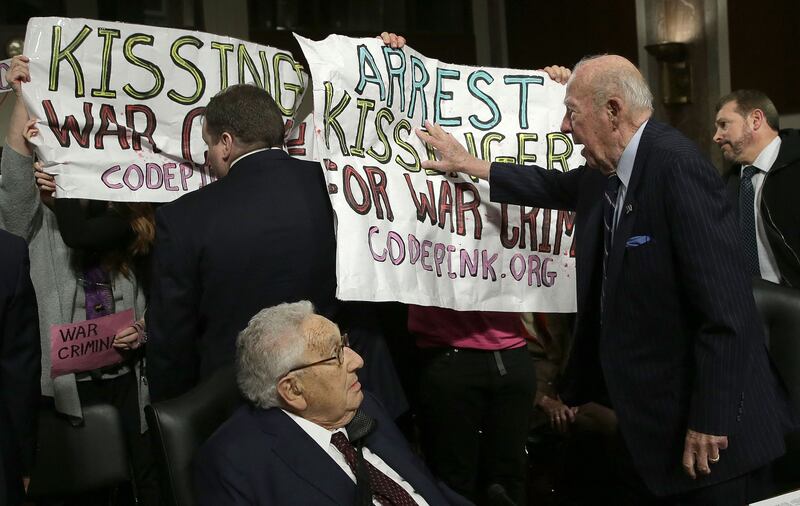 Former US secretary of state George Shultz pushes away protesters shouting 'Arrest Henry Kissinger for war crimes', as Mr Kissinger looks on, in Washington, in 2015. AFP