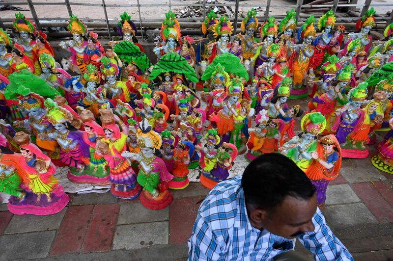 A vendor waits for customers as he sits next to idols of Krishna along a roadside in New Delhi. AFP