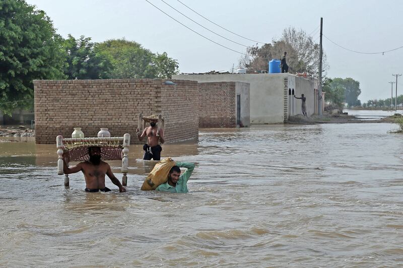 Flood affected people carry their belongings as they wade through flood water in Bahawalnagar of Punjab province on August 27, 2023.  Families waded through water and cattle were loaded onto boats in a mass evacuation of around 100,000 people in Pakistan's Punjab province, officials said on August 23.  (Photo by Shahid Saeed Mirza  /  AFP)