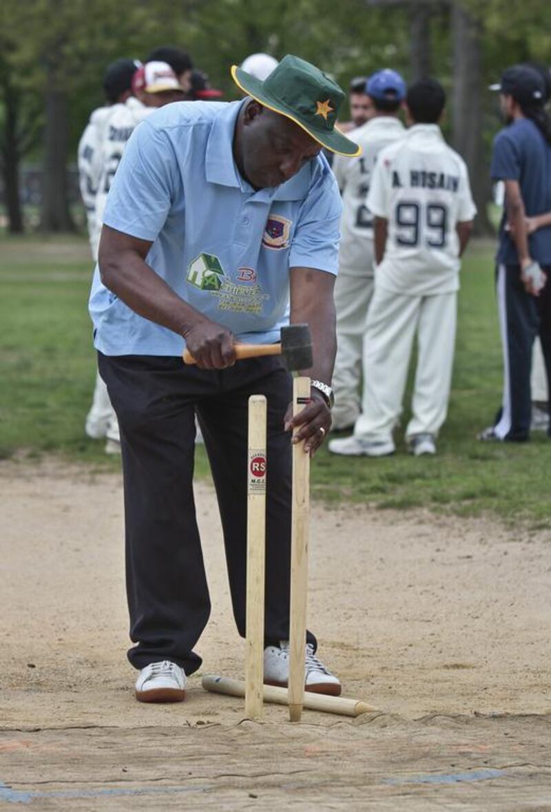 In this May 12, 2014 photo, cricket umpire Carl Whatley uses a hammer to set up wickets for a New York City Public School Athletic League (PSAL) cricket match between John Adams and Midwood high schools. Bebeto Matthews / AP