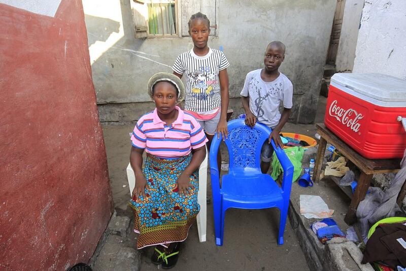 Siblings Comfort, left, Silvia, centre and Melvin Yeah pose for a family portrait at their home in Monrovia, Liberia. The empty chair symbolises their mother, who died of the Ebola virus disease during an outbreak of the disease in 2014. Ahmed Jallanzo / EPA