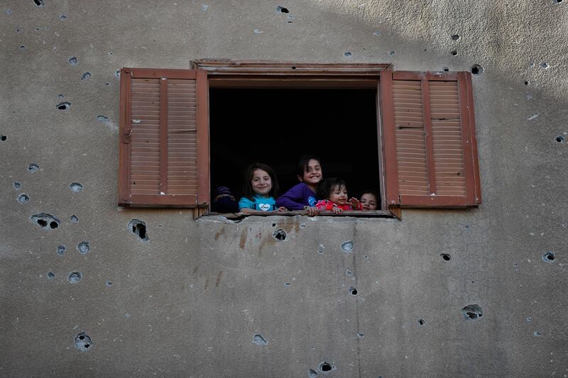 In this Thursday, April 5, 2018 photo, children look from the window of their house that was damaged last summer during fighting between U.S.-backed Syrian Democratic Forces fighters and Islamic State militants, in Raqqa, Syria. Six months after IS was driven out, residents of Raqqa feel they have been abandoned as the world moves on. They are trying to rebuild but fear everyone around them: the Kurdish-led militia that administers the majority Arab city; Syrian government forces nearby; gangs who kidnap or rob whoever shows signs of having money; and IS militants who may still be hiding among the people. (AP Photo/Hussein Malla)