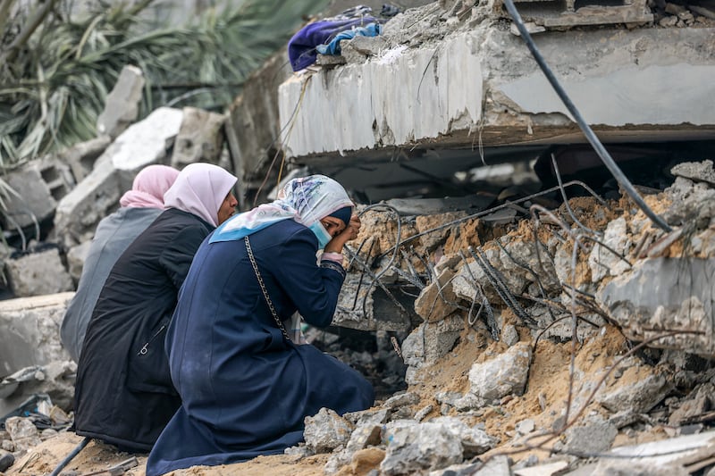 Palestinian women huddle over a spot where a relative is believed to be trapped under debris, in Rafah. AFP