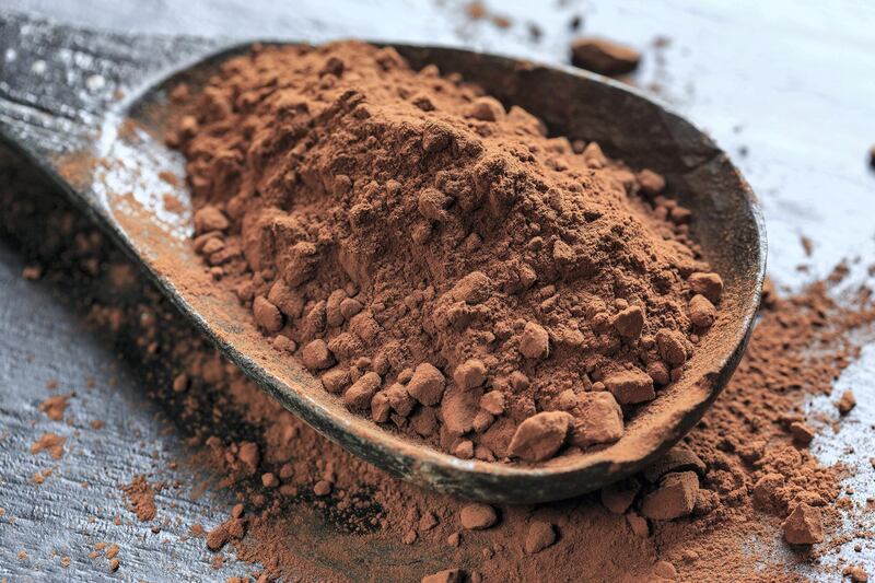 Cocoa powder in a wooden spoon on black background, close-up