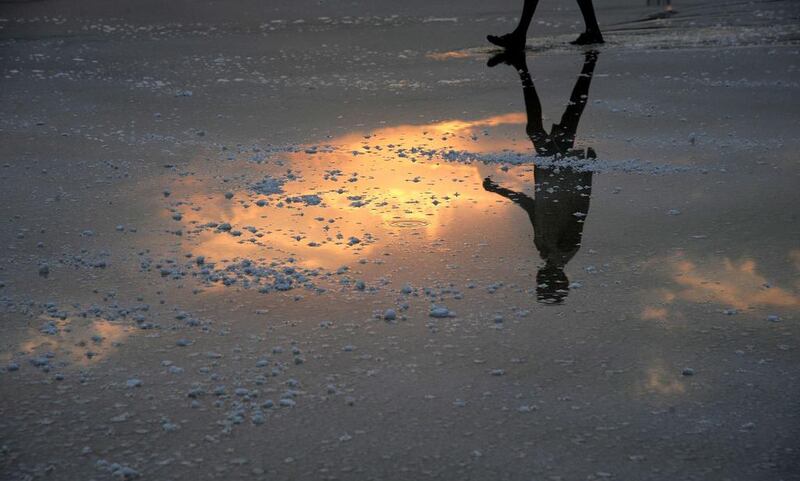 An Indian labourer and the rising sun are reflected in water as arrives to work on a salt pan on the outskirts of Mumbai. Vast tracts of over 3,000 acres of “salt pan” lands in Mumbai might disappear soon as a proposal to convert them to housing projects for displaced squatters is in the offing. Indranil Mukherjee / AFP