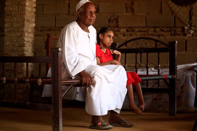 Nafisa Ali Al Awad, 8, who is unable to walk or speak, a handicap believed to be caused by her exposure to gold mining residues, with her father. AFP