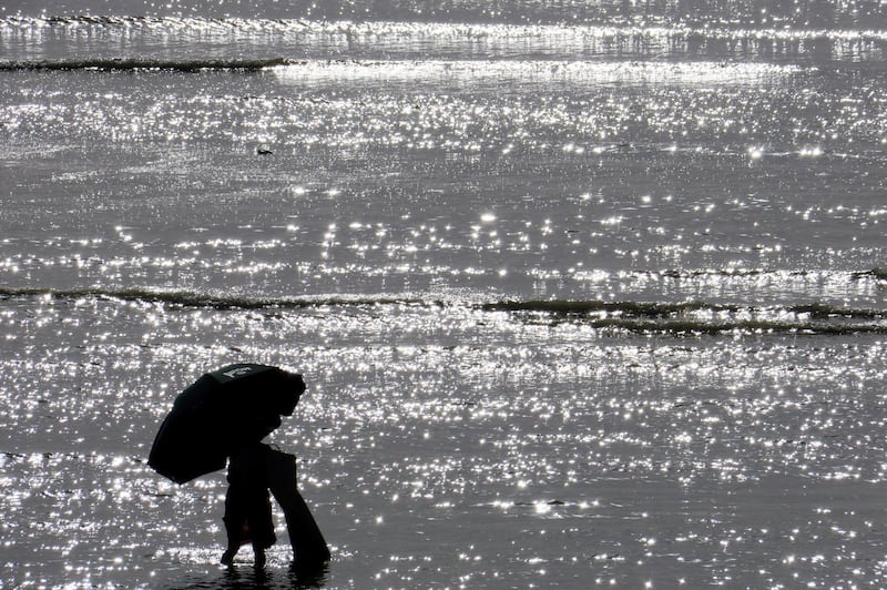 A woman escapes with her beach umbrella and bath towel during the rising tide as the heatwave hits France, in Cayeux-sur-Mer, France.  Reuters