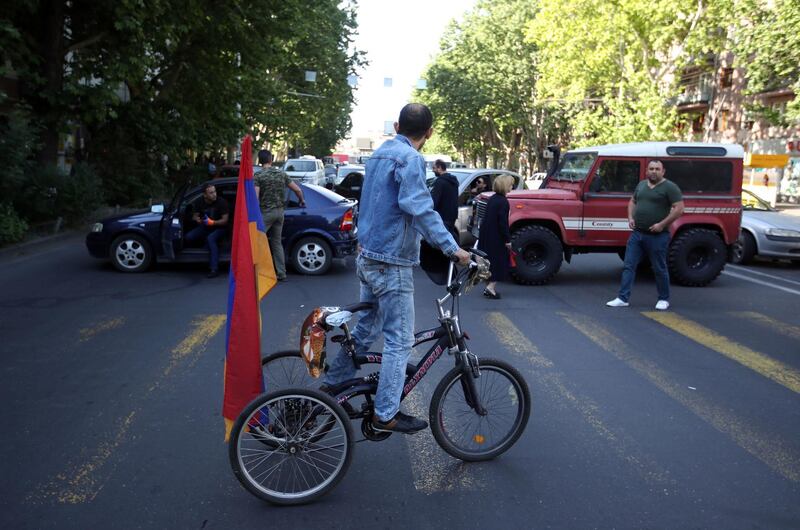 A supporters of the opposition lawmaker Nikol Pashinian rides a tricycle as he looks at people blocking a road in Yerevan on Wednesday, May 2, 2018. Pashinyan has urged his supporters to block roads, railway stations and airports on Wednesday after the governing Republican Party voted against his election as prime minister. (AP Photo/Thanassis Stavrakis)