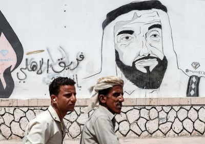 A picture taken on August 8, 2018 during a trip in Yemen organised by the UAE's National Media Council (NMC) shows Yemeni men riding in a motorcycle past a mural depicting the late UAE founder and president Sheikh Zayed bin Sultan al-Nahyan, along a street in the southeastern port city of Mukalla, the capital Hadramawt province. (Photo by KARIM SAHIB / AFP)
