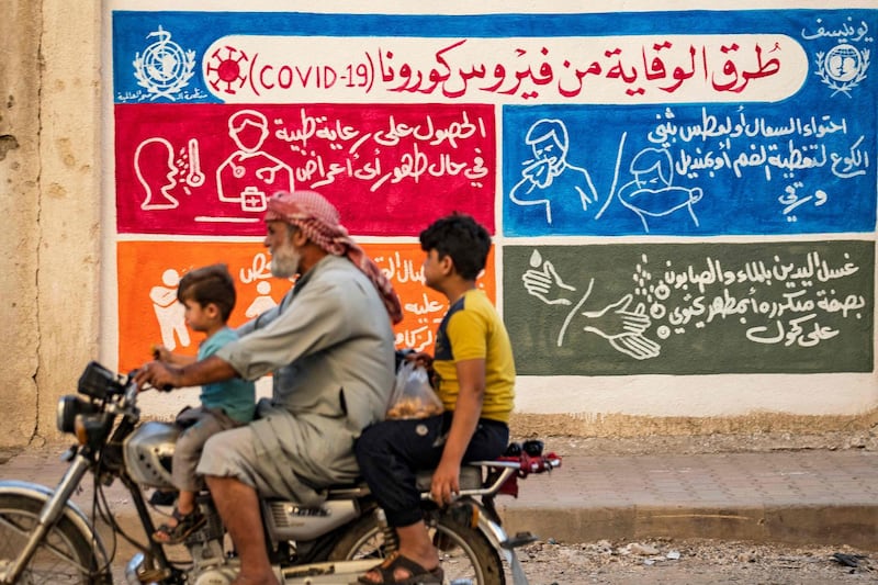 Syrians ride a motorbike past a mural painted as part of an awareness campaign by the United Nations International Children's Emergency Fund (UNICEF) and World Health Organization (WHO) intitative, bearing instructions on protection from COVID-19 in the Kurdish-majority city of Qamishli of Syria's northeastern Hasakeh province, after a spike in infections in the area. AFP