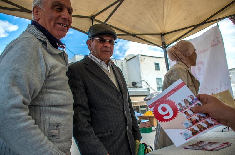 A volunteer of an independent local party gives electoral leaflets to residents in l'Ariana, outside Tunis, Friday, May 4 2018. Tunisia is hoping to break through barriers with its first local elections since its Arab Spring revolution: They could bring the first woman mayor of the capital, the first Jewish official with an Islamist party and new flock of mayors with greater powers. (AP Photo/Hassene Dridi)