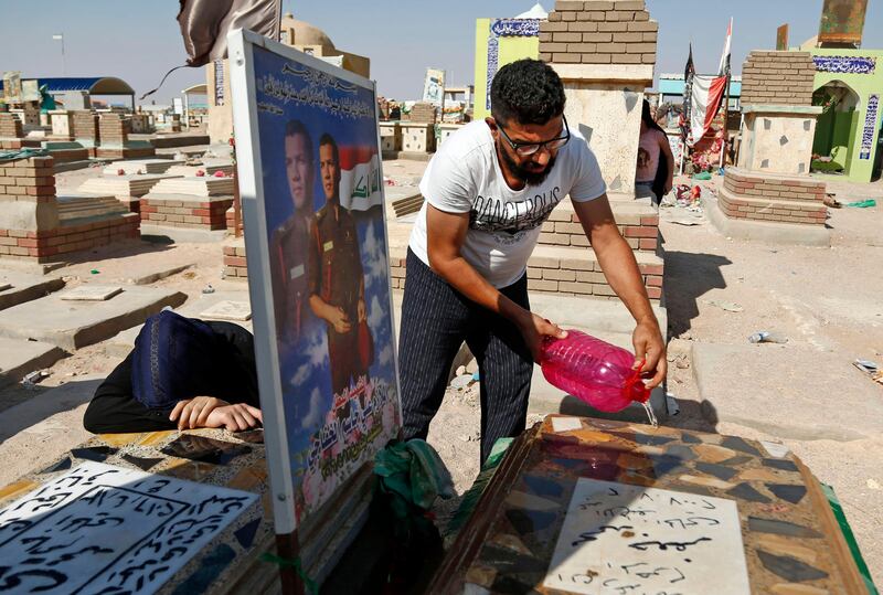 Iraqis clean and mourn over the graves of relatives killed in the combat against the Islamic State (IS) group at the Wadi al-Salam cemetary in the Shiite holy city of Najaf on the first day of the Eid al-Adha holiday on September 1, 2017. / AFP PHOTO / Haidar HAMDANI